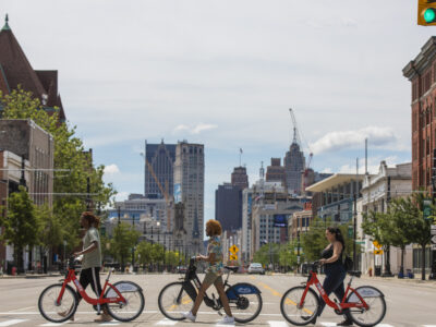 Group of three friends crossing crosswalk with their bikes in tow, located at Detroit's Brush Patk